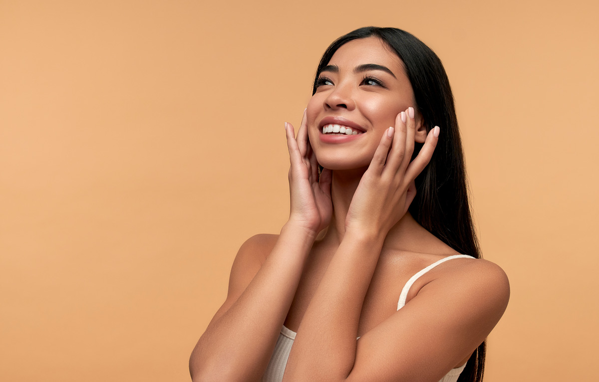 A smiling woman with her hands on her face in front of a beige background in Richmond.