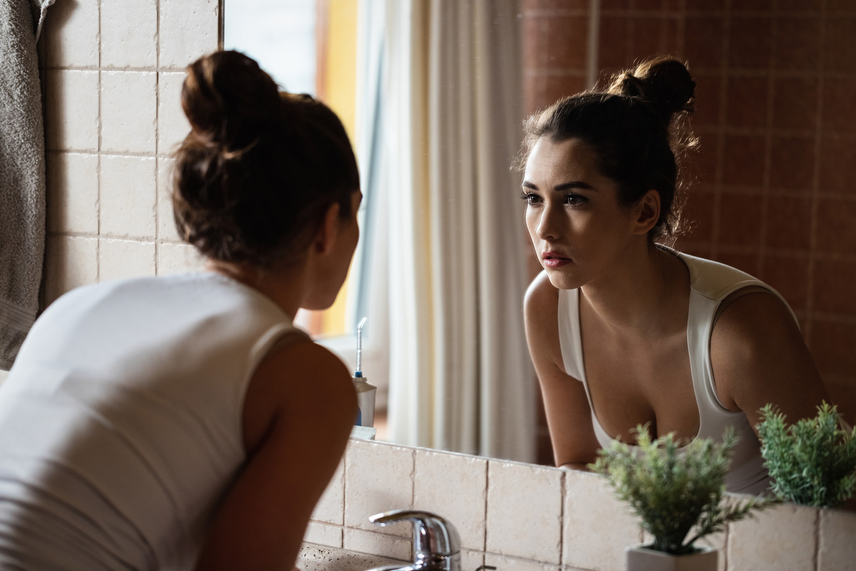 A woman in a white shirt looking at her reflection in a mirror in Richmond.